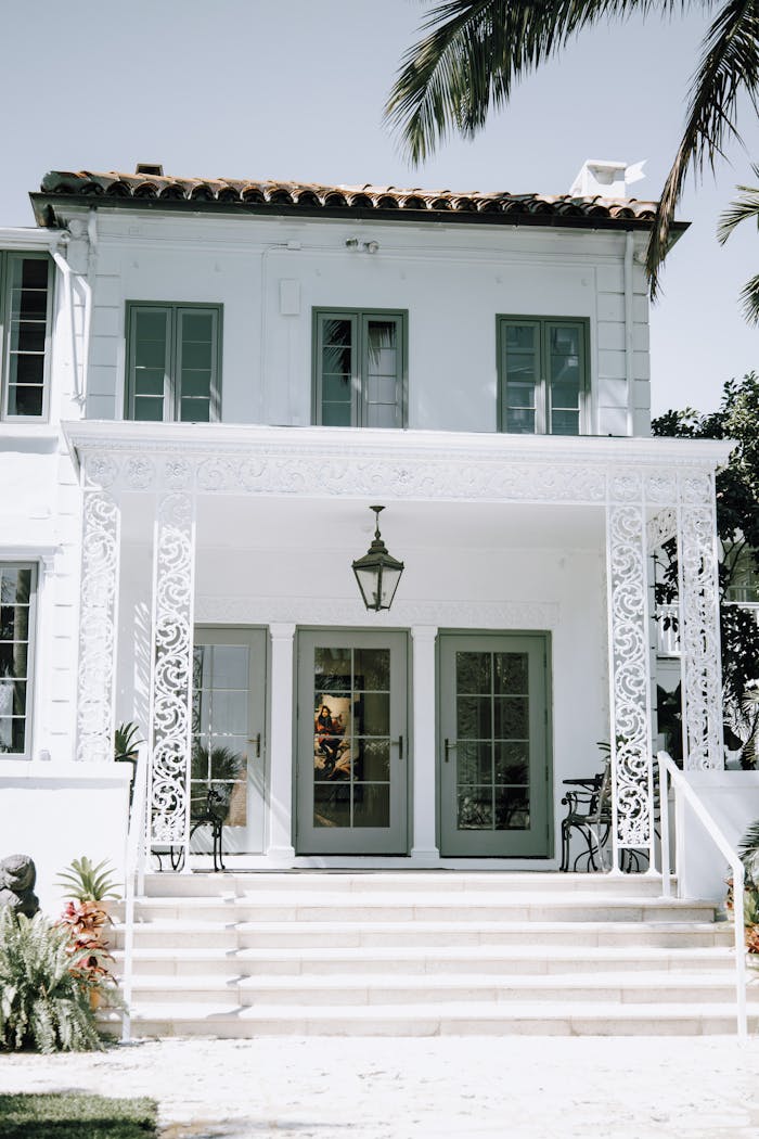 A luxurious mansion entrance showcasing classic architecture with decorative ironwork and tropical surroundings.